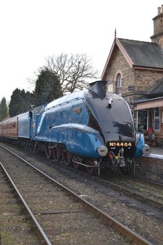 a blue and black train traveling down tracks next to a brick building with a clock tower