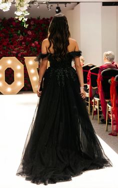 the back of a woman in a black dress standing on a stage with red chairs