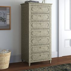 a tall chest of drawers sitting next to a wall with pictures on it and a basket in the corner