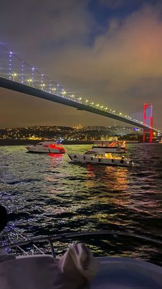 boats in the water near a bridge at night with bright lights on it's sides