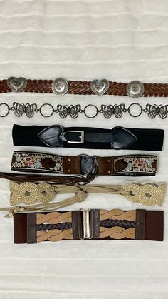 four different belts are laid out on a white sheet with silver buckles and chains