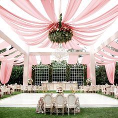 an outdoor wedding reception setup with pink drapes and chandelier hanging from the ceiling