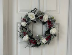 a wreath with white roses and greenery hanging on a door