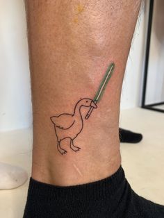 a small tattoo on the ankle of a person with a duck holding a green stick