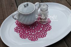 a white plate with a tea pot on it and doily next to the cup