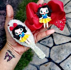 a hand holding two little dolls on top of it's fingers and one is wearing a red bow