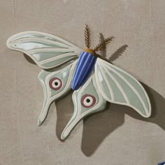 a ceramic butterfly decoration on the wall with eyes and nose painted on it's wings