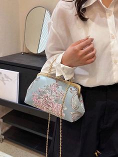 a woman wearing a white shirt and black pants holding a blue purse with pink flowers on it