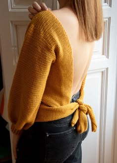 the back of a woman's sweater with a tie around her waist, standing in front of a door