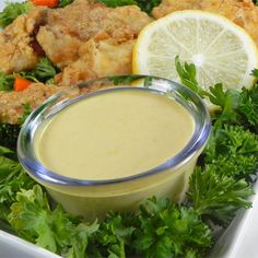 a white plate topped with chicken and salad next to a bowl of dressing on top of lettuce