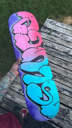 a person holding up a skateboard with graffiti on it's side in front of a park bench