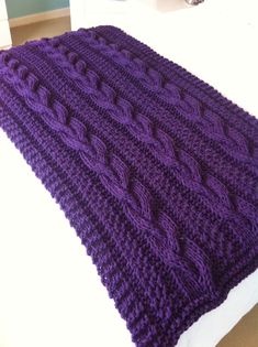 a purple knitted blanket sitting on top of a bed