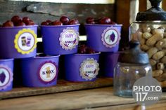 several purple buckets filled with nuts sitting on top of a wooden table next to a jar