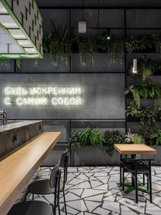 an indoor cafe with plants growing on the wall and wooden tables in front of it