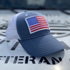 Slate & White Mesh-Back Trucker Hat Custom Made Right Here In The USA! 🇺🇸 This slate fabric and white mesh trucker hat has an oversized full-color American flag and branded side panel. ✅ Our classic trucker hats are structured with a higher profile ✅ Pre-curved visor ✅ Snap-back closure ✅ Branded side panel ✅ Moisture-wicking sweatband ✅ Classic top button ✅ Superior quality, comfort, and American craftsmanship. Trucker Baseball Cap With Flat Brim For Baseball Season, White Adjustable Trucker Dad Hat, Summer Trucker Snapback Hat With Six-panel Design, Summer Trucker Snapback Hat Six-panel, Trucker Style Baseball Cap For Baseball Season, Trucker Hat With Flat Brim For Sports, Patriotic Baseball Cap For Outdoor, White Cap For Memorial Day, Outdoor Cap Made In Usa