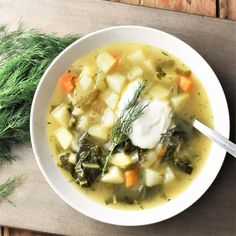 a white bowl filled with vegetable soup on top of a wooden table next to a spoon