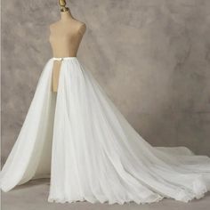 a white wedding dress on a mannequin with a long train and sheer tulle skirt