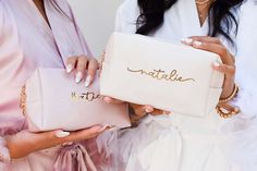 two women holding pink bags with gold lettering on the side and one is holding a white purse