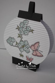 a card with flowers and a butterfly on the front, sitting on top of a black stand