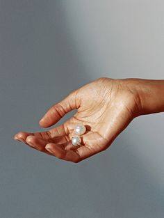 a woman's hand with a pearl ring on her left thumb, against a gray background