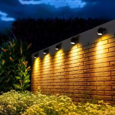 three lights are on the side of a brick wall next to some flowers and bushes