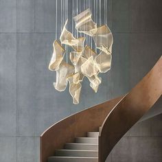 a spiral staircase with chandelier hanging from it's sides in front of a gray wall