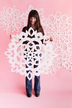 a girl holding a paper snowflake in front of a pink background with the text,