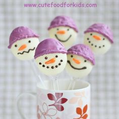 four marshmallow snowman pops in a mug with purple hats and scarf on them