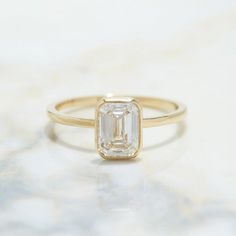 a ring with an emerald cut diamond on it sitting on a marble countertop next to a white background