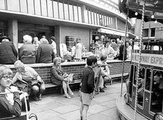 black and white photograph of people sitting on benches in front of a double decker bus