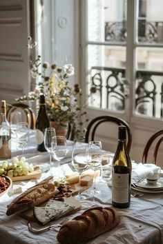 a table with bread, cheese and wine on it in front of a large window