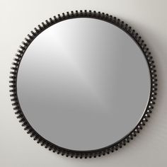 a round mirror hanging on the wall with black beaded trim around it's edges