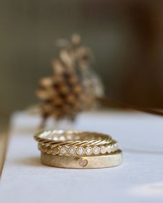 two wedding rings sitting on top of a table next to a pine cone with a bird in the background