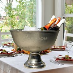 a silver bowl filled with bottles of wine on top of a table next to plates and utensils