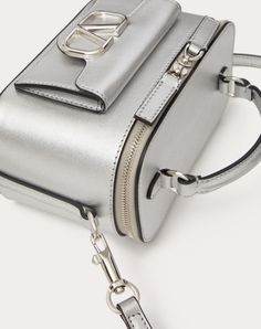 Valentino Garavani Locò mini handbag in metallic calfskin with metallic VLogo Signature detail. Can be worn over the shoulder/crossbody or carried as a handbag thanks to the handle and the adjustable and removable shoulder strap. - Palladium-finish logo and hardware - Zip closure - Nappa leather lining. Interior: one card slot - Outside pocket with magnetic closure - Adjustable and removable leather shoulder strap - Shoulder strap drop length: min 52.5 cm to max 57.5 cm / min. 20.7 in. to max. 2 Luxury Shoulder Box Bag With Silver-tone Hardware, Luxury Box Shoulder Bag With Silver-tone Hardware, Luxury Box Bag With Silver-tone Hardware, Luxury Silver-tone Hardware Box Shoulder Bag, Luxury Box Bag Satchel With Silver-tone Hardware, Luxury Box Bag With Silver-tone Hardware Satchel, Luxury Silver Shoulder Bag With Gold-tone Hardware, Silver Designer Shoulder Bag With Detachable Strap, Luxury Silver Crossbody Shoulder Bag