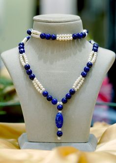 a blue and white necklace with pearls on a mannequin head stand in front of a glass display case