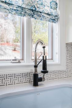 a kitchen sink under a window next to a faucet and windowsill with roman blinds