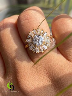 a woman's hand with a diamond ring on top of her finger and grass in the background