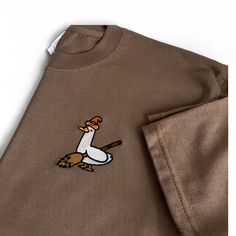 Brown organic t shirt with an embrodiered silly goose  Witchy Silly Goose T- Shirt with Halloween theme embroidery design. 👻 Unisex relaxed fit  ✨Classic silly goose dressed and ready for Haloween! Witchy goose✨ If you would like a size or colour that you can't see here then please don't hesitate to message us as we would love to try to accommodate your request as best we can 😊  ✨By buying a little something from us you will supporting a small business (entirely ran by just 2 lovely ladies ️)! Casual Embroidered Fall T-shirt, Casual Embroidered T-shirt For Fall, Halloween Embroidered Cotton Tops, Halloween Cotton Embroidered Tops, Casual Embroidered Halloween T-shirt, Embroidered Cotton Tops For Halloween, Halloween Embroidered Crew Neck T-shirt, Halloween Cotton Top With Embroidered Graphics, Fall Embroidered Graphic Tee