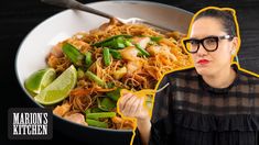 a woman holding a fork in front of a bowl of food with noodles and vegetables