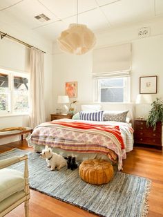 a bed room with a neatly made bed and two small dogs on the rugs