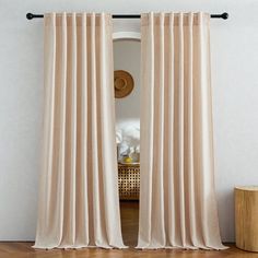 a room with a wooden floor and beige curtains hanging on the wall next to a mirror