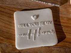 a cookie that says, will you be my maid of honor? on top of a wooden table