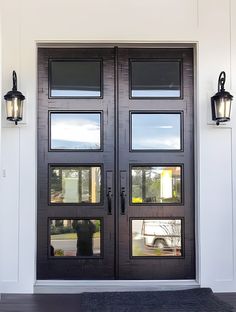 a black double door with two lights on each side and an entrance mat in front