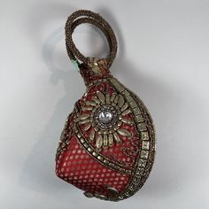 Add a touch of elegance to your outfit with this stunning red and gold brocade potli bag. This bag features intricate beaded accents and a gold handle/strap for added flair. The zippered closure keeps your belongings secure while the compact size makes it perfect for any occasion. This vintage Indian-themed clutch purse is made of high-quality fabric that gives it a timeless look. The beige lining adds a touch of sophistication, while the red and gold hardware color combination gives it a modern twist. Whether you're heading to a formal event or a casual gathering, this wristlet is the perfect accessory to complete your look.