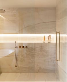 a modern bathroom with marble walls and flooring, shower head, and bathtub