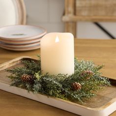 a lit candle sitting on top of a tray with pine cones and greenery around it