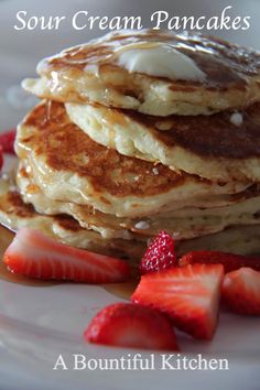 a stack of pancakes with syrup and strawberries on a white plate that says sour cream pancakes