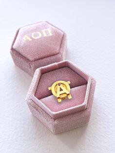 an open pink box with a gold ring in it sitting on a white table top