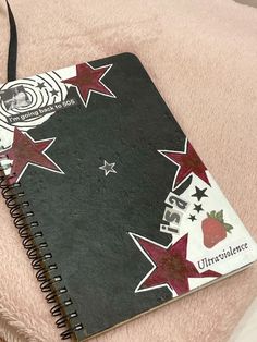 a black notebook with red and white stars on it sitting on top of a pink blanket